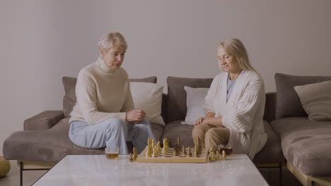 Two-Senior-Women-Playing-Chess-Sitting-On-Sofa-At-Home-1