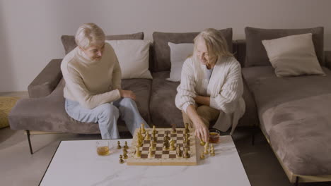 Two-Senior-Women-Playing-Chess-Sitting-On-Sofa-At-Home-4