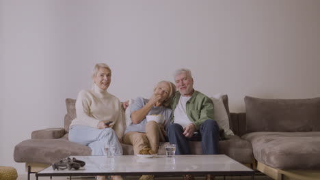 Gruppe-Von-Drei-Senioren,-Die-Fernsehen,-Während-Sie-Zu-Hause-Auf-Dem-Sofa-Sitzen