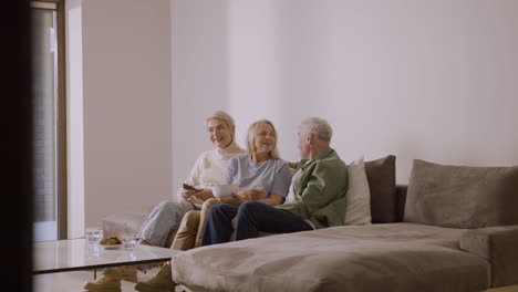 Gruppe-Von-Drei-Senioren,-Die-Fernsehen-Und-Miteinander-Reden,-Während-Sie-Zu-Hause-Auf-Dem-Sofa-Sitzen