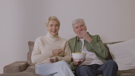 Seniorenpaar-Isst-Karamell-Popcorn-Und-Sieht-Fern,-Während-Es-Zu-Hause-Auf-Dem-Sofa-Sitzt