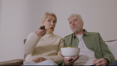 Glückliches-älteres-Paar,-Das-Karamellpopcorn-Isst-Und-Fernsieht,-Während-Es-Zu-Hause-Auf-Dem-Sofa-Sitzt
