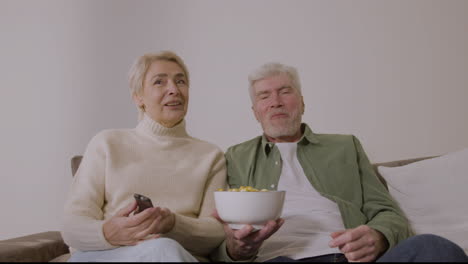 Glückliches-älteres-Paar,-Das-Karamellpopcorn-Isst-Und-Fernsieht,-Während-Es-Zu-Hause-Auf-Dem-Sofa-Sitzt-1