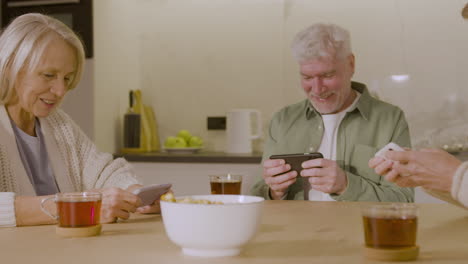 Three-Senior-Friends-Playing-Game-Using-Their-Mobile-Phones-At-Home-1
