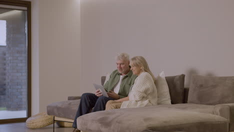 älteres-Paar-Sitzt-Zu-Hause-Auf-Dem-Sofa-Mit-Digitalem-Tablet