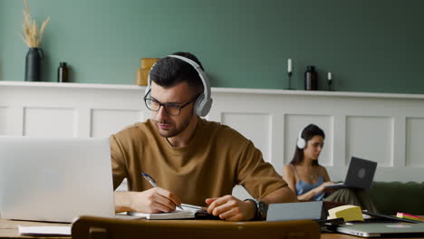 Close-Up-View-Of-A-Student-Using-Headphones-And-Opening-Laptop-Sitting-At-Table