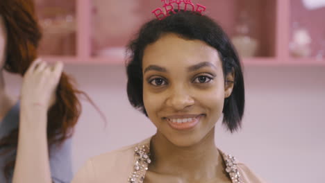 Close-Up-View-Of-Woman-With-Headdresses-And-Holding-Cardboard-Phrase-Dancing-In-A-Pink-Room-Celebrating-A-Bachelorette-Party