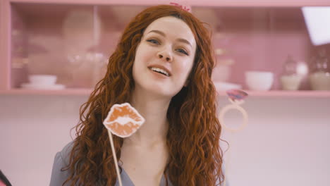 Close-Up-View-Of-Redhead-Woman-With-Headdresses-And-Holding-Cardboard-Decoration-Dancing-In-A-Pink-Room-Celebrating-A-Bachelorette-Party