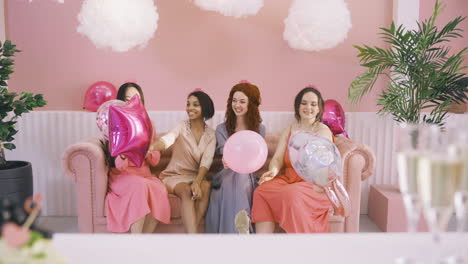 Vorderansicht-Von-Vier-Frauen-Mit-Kopfbedeckungen,-Die-Ballons-Halten-Und-Auf-Dem-Sofa-Sitzen-Und-Reden