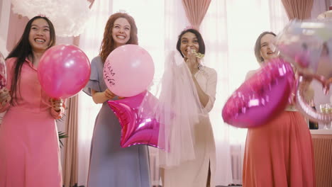 Front-View-Of-Four--Women-With-Headdresses-Jumping-And-Holding-Ballons-While-They-Wait-For-Their-Friend-To-Celebrate-The-Bachelorette-Party