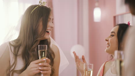 Close-Up-View-Of-Bachelor-Girl-With-Headdress-Holding-Champagne-Crystal-Glasses-And-Talking-With-Her-Friends