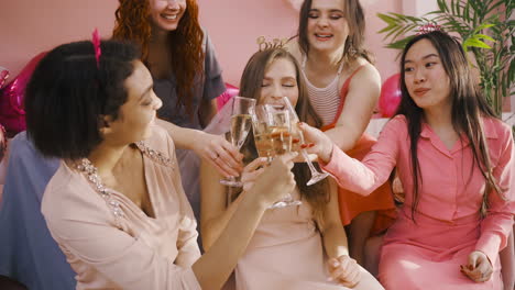 Side-View-Of-Group-Of-Friends-And-Bachelor-Girl-Holding-Champagne-Crystal-Glasses-While-Dancing-Sitting-On-Sofa