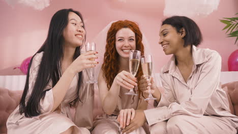 Front-View-Of-Three-Multiethnic-Friends-Toasting-With-Champagne-Sitting-On-Sofa-Celebrating-Bachelorette-Party-1