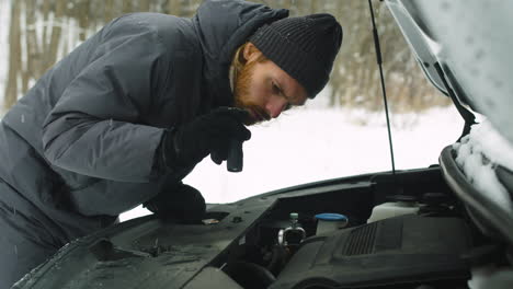 Man-Stuck-In-The-Winter-Forest-Holding-A-Torch-And-Checking-His-Car-Engine-Problem-1