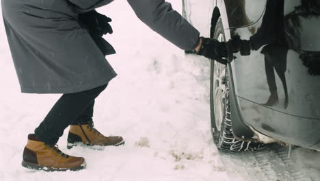 Close-Up-Of-An-Unrecognizable-Man-Checking-Car-Wheels-During-A-Snowy-Winter-Day