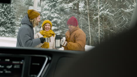 Cheerful-Friends-Drinking-Hot-Tea-In-A-Snowy-Forest-During-A-Winter-Road-Trip
