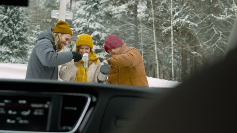 Cheerful-Friends-Drinking-Hot-Tea-In-A-Snowy-Forest-During-A-Winter-Road-Trip-1