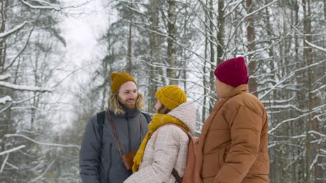 Side-View-Of-Three-Friends-In-Winter-Clothes-Talking-About-Something-They-Have-Seen-In-A-Winter-Forest