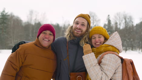 Front-View-Of-Three-Friends-In-Winter-Clothes-Smiling-At-Camera-In-Winter-Forest