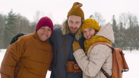 Front-View-Of-Three-Friends-In-Winter-Clothes-Smiling-At-Camera-In-Winter-Forest-1
