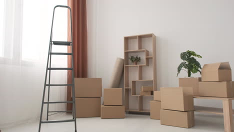 Zoom-Out-Shot-Of-Moving-Boxes-And-Ladder-In-Empty-Room-Of-New-Home