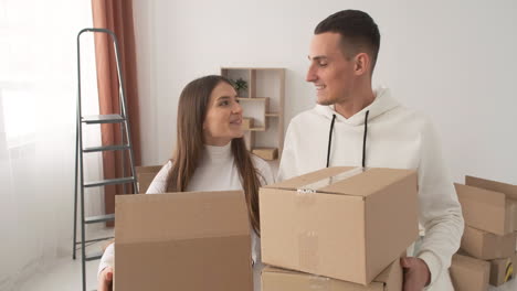 Happy-Couple-Moving-To-New-Place-Holding-Cardboard-Boxes-And-Walking-Together-In-Empty-Flat-1