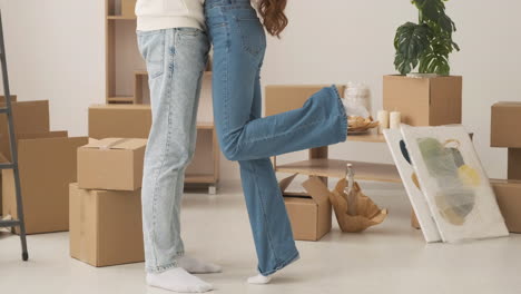 Close-Up-Of-Legs-Of-Unrecognizable-Couple-Standing-Among-Cardboard-Boxes-In-New-House