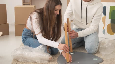 Young-Couple-Moving-Into-New-House-Sitting-On-Floor-And-Assembling-Coffee-Table-Together-3