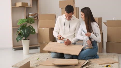 Front-View-Of-A-Young-Couple-In-A-New-House-Sitting-On-The-Carpet-Assembling-A-Furniture