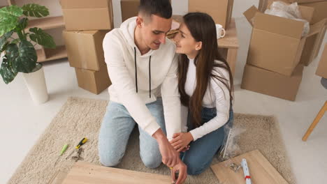 Top-View-Of-A-Young-Couple-In-A-New-House-Sitting-On-The-Carpet-Assembling-A-Furniture