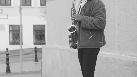 Black-And-White-View-Of-A-Sax-Case-With-Coins-On-The-Floor-And-A-Man-In-Jacket-Playing-Sax-In-The-Street