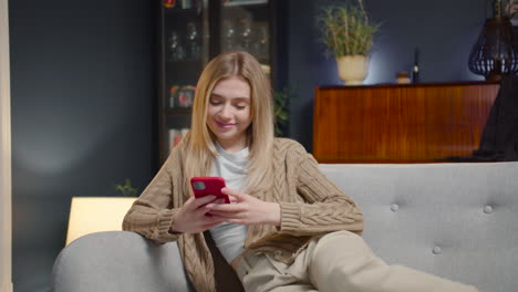 Happy-Young-Woman-Chatting-On-Smartphone-And-Laughing-While-Sitting-On-A-Couch-At-Home-1