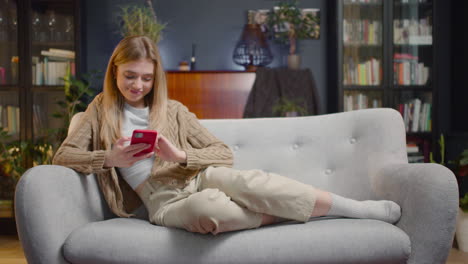 Glückliche-Junge-Frau,-Die-Smartphone-Verwendet,-Während-Sie-Zu-Hause-Auf-Einer-Couch-Liegt