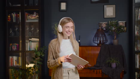 Happy-Young-Woman-With-Headphones-Listening-Music-On-Tablet-And-Dancing-In-Living-Room-At-Home