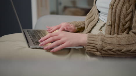 Close-Up-Of-An-Unrecognizable-Woman-Typing-On-Laptop-Computer-While-Sitting-On-Couch-At-Home