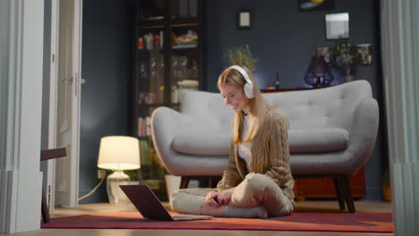 Happy-Young-Woman-With-Wireless-Headphones-Watching-A-Funny-Movie-On-Laptop-Computer-While-Sitting-On-Floor-At-Home