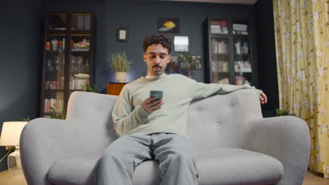 Verkleinern-Sie-Die-Ansicht-Eines-Jungen-Mannes,-Der-Ein-Smartphone-Benutzt,-Während-Er-Zu-Hause-Auf-Einer-Couch-Sitzt