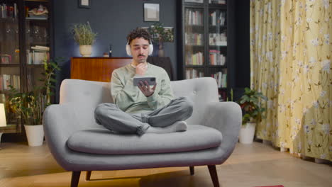 Young-Man-Watching-Comic-Movie-On-Smartphone-While-Sitting-With-Crossed-Legs-On-Couch-At-Home
