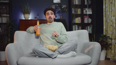 Young-Man-Watching-Unexpected-Movie-Scene-On-Tv-While-Eating-Chips-And-Drink-Soda-Sitting-With-Crossed-Legs-On-Couch-At-Home-1