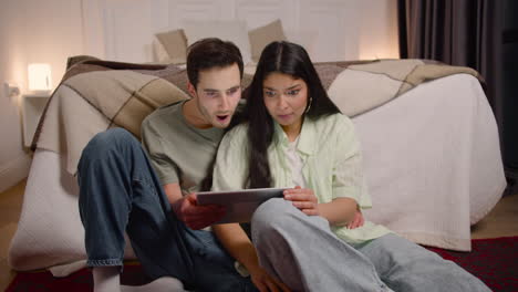 Couple-Watching-Unexpected-Movie-Scene-On-Tablet-While-Sitting-On-The-Floor-At-Home-1
