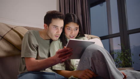 Bottom-View-Of-Couple-Watching-Interesting-Movie-On-Tablet-While-Sitting-On-The-Floor-At-Home