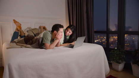 Couple-Watching-Interesting-Movie-On-Latop-Lying-In-Bed-At-Home
