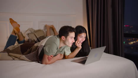 Couple-Watching-Interesting-Movie-On-Laptop-Lying-In-Bed-At-Home