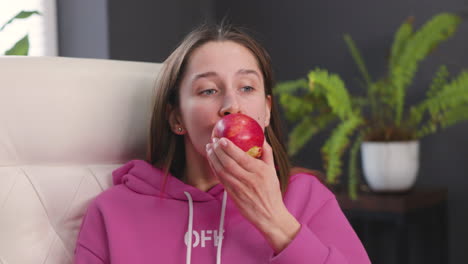 Young-Woman-Sitting-At-Desk-And-Eating-A-Red-Apple