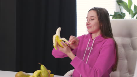 Mujer-Joven-Feliz-Sentada-En-El-Escritorio-Pelando-Y-Comiendo-Plátano
