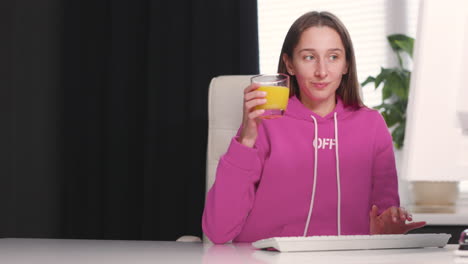 Young-Woman-Drinking-An-Healthy-Orange-Juice-While-Using-Desktop-Computer-At-Office-1