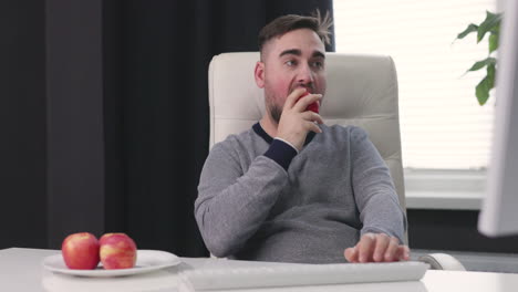 Hombre-Hambriento-Sentado-En-El-Escritorio-Escribiendo-En-El-Teclado-Y-Comiendo-Manzanas