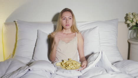 Blonde-Girl-Sitting-In-The-Bed-And-Eating-Potato-Chips
