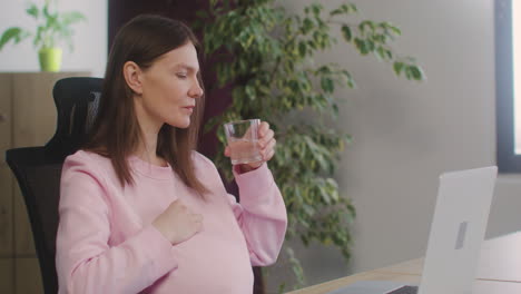 Mujer-Embarazada-Acariciando-Su-Vientre-Y-Bebiendo-Agua-Mientras-Trabaja-En-La-Oficina