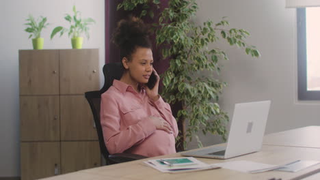 Pregnant-Woman-Talking-On-Her-Mobile-Phone-And-Caressing-Her-Belly-While-Working-In-The-Office-1